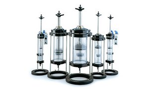 Conjunto de cinco columnas cromatográficas con diferentes alturas, cada una con una sección central transparente, bases y tapas negras, y algunas con válvulas azules.