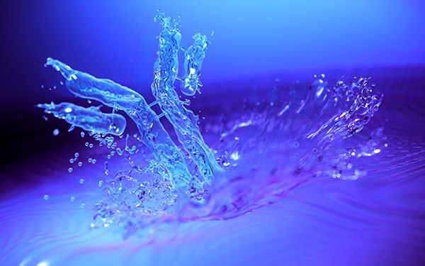Reduced Viscosity in Highly Concentrated Protein Therapeutics Salpicaduras dinámicas de agua con gotitas suspendidas en el aire e iluminadas por luz azul que crean una escena serena y fluida.