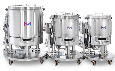 Tres biorreactores de acero inoxidable de diferentes tamaños en soportes con ruedas, cada uno con un logotipo ‘M’ azul y rosa en la parte delantera. Tres biorreactores de acero inoxidable de diferentes tamaños en soportes con ruedas, cada uno con un logotipo ‘M’ azul y rosa en la parte delantera.