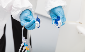 Manos con guantes azules que trabajan con pequeños conectores eléctricos. La persona lleva una bata blanca de laboratorio, lo que sugiere un entorno profesional o de laboratorio. Hay cables de colores unidos a los conectores.