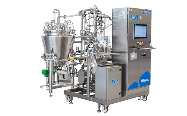 Cogent® Process-Scale TFF System Máquina industrial compleja, principalmente gris con detalles azules, con un gran cuenco de mezcla de acero inoxidable, un panel de control con botones y una pantalla, y otras piezas mecánicas como tuberías y válvulas.