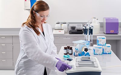 Western blotting using the SNAP i.d.® 2.0 protein detection system Profesional con bata de laboratorio y guantes morados está trabajando con un dispositivo de inmunodetección de membrana en un laboratorio bien equipado, rodeado de diversos equipos y suministros de laboratorio, destacando la precisión y el cuidado involucrados en los procesos de inmunodetección.