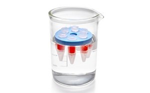 Vaso de precipitados de laboratorio transparente lleno de líquido incoloro, que contiene un pequeño recipiente cilíndrico con un líquido rojo en su interior. El recipiente está rematado con una tapa azul, que flota en la superficie del líquido del vaso de precipitados. El vaso tiene marcas de medición en el lateral que indican su volumen.
