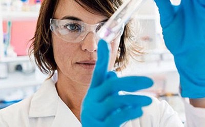 Professional Laboratory Scientist Conducting Experiment La imagen muestra a una mujer en un laboratorio examinando atentamente un tubo de ensayo que contiene un líquido transparente.