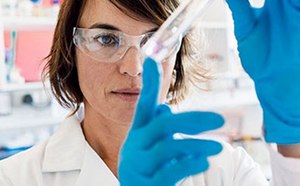 Una científica o técnica de laboratorio con bata blanca y guantes azules participa en un experimento o análisis en un entorno de laboratorio.