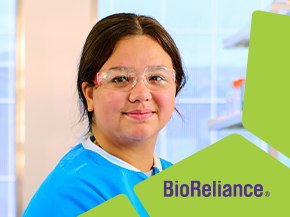 A laboratory technician wearing a blue lab coat is standing in a bright laboratory setting. The background features laboratory equipment and shelves. In the lower right corner, there is a green banner with the text 'BioReliance.'