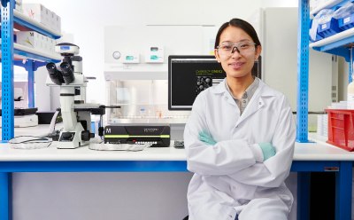 Luminex<sup>®</sup> 装置の横に立ってMILLIPLEX<sup>®</sup> マルチプレックスバイオマーカーアッセイ試薬の箱を持っている研究者と、後ろのベンチ上にあるSMCxPRO<sup>®</sup> 超高感度イムノアッセイ装置