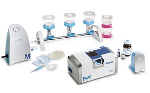 A laboratory setup featuring the EZ-Stream Pump and EZ-Flow System from Millipore, with clear filtration cups connected by a metallic tube, various vials of liquids, and other accessories arranged neatly on a white background.