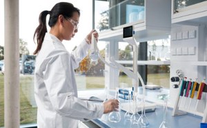 Female scientist in a white lab coat is filling volumetric flasks with ultrapure water from a Q-POD dispenser in a modern lab setting with a bright and organized workspace