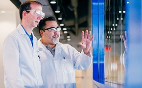 Un científico explicando la reciente innovación a otro científico frente a una ventana azul