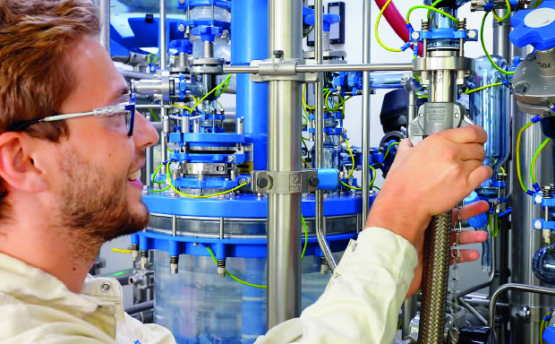 Lipids CDMO A male production worker in the Schaffhausen pilot plant facilities is connecting a solvent hose to the reactor system, preparing for upcoming manufacturing activities.