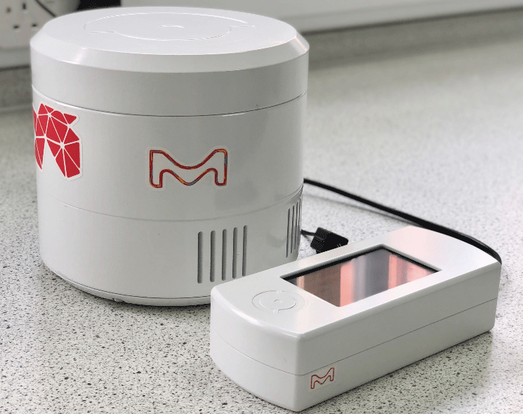 LightOX Photoreact 365 A close-up view of the LightOX Photoreact 365, featuring a round white photoreactor unit with the M logo in red, alongside a rectangular control device with a digital display. The devices are placed on a light-colored laboratory countertop, with a power cable connecting them.