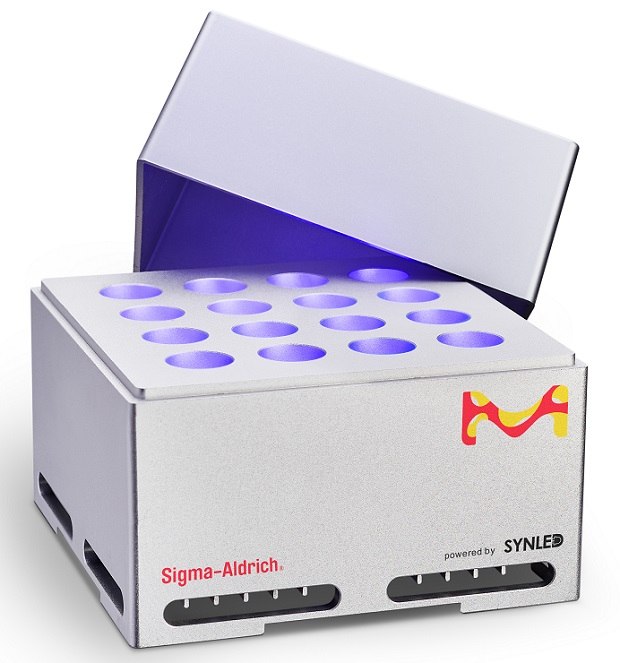 SynLed Parallel Photoreactor 2.0 SynLED Parallel Photoreactor 2.0 against a white background. The device is a light grey cuboidal box with its cover partially open, revealing 16 vials illuminated by a 1 W blue LED centered at 467.5 nm, equipped with a 45° lens. The side facing the viewer displays a vibrant M logo in yellow and red at the top right corner.