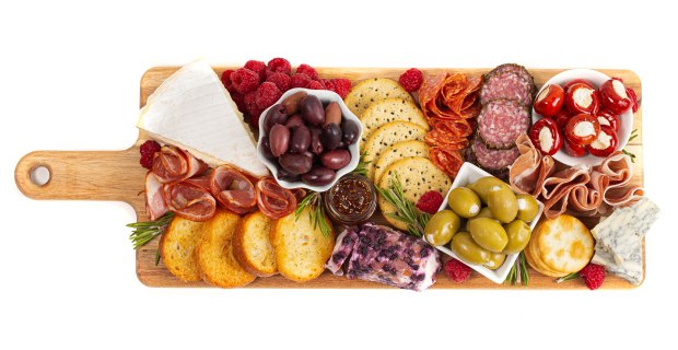Charcuterie board with a selection of savory snacks and preserved foods. Displayed on a charming wooden board equipped with a convenient handle, the charcuterie platter presents a delightful assortment of savory delicacies. The carefully curated selection includes a variety of preserved meats, enticing olives, flavorful peppers, luscious berries, crisp crackers, and an array of delectable cheeses.