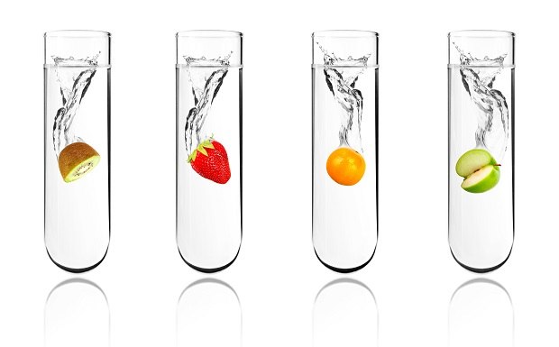 Navigating Global Natural Flavor Definitions and Regulations Four test tubes contain water and various fruits – kiwi, strawberry, orange, and green apple – with splashes inside, representing natural flavors for assessment.