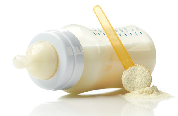 Infant feeding baby bottle with formula A baby bottle filled with milk, accompanied by a yellow measuring scoop and powdered formula on a white surface
