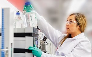 Lab worker looking at a bottle of fluid on a shelf.